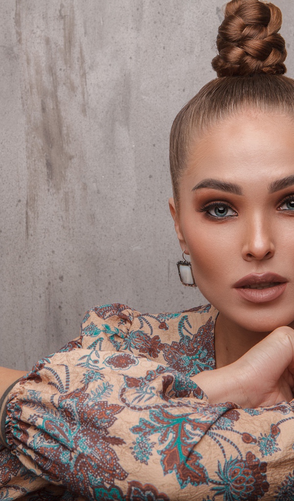 Молодая девушка с прической на голове на фоне стены