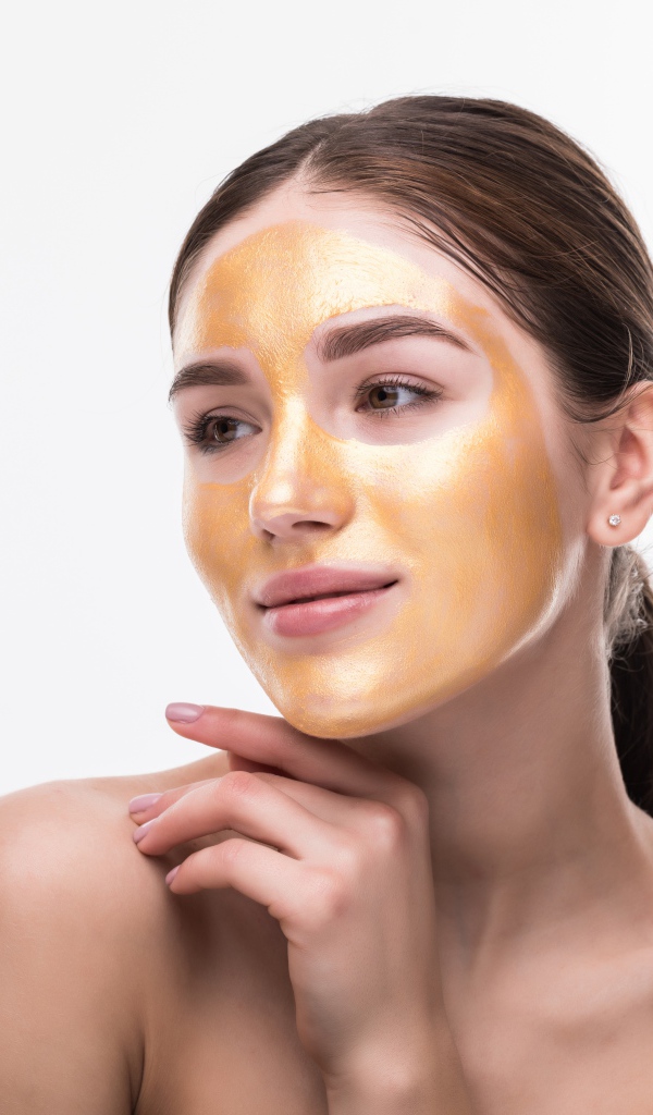 Молодая девушка без макияжа с золотой маской на лице