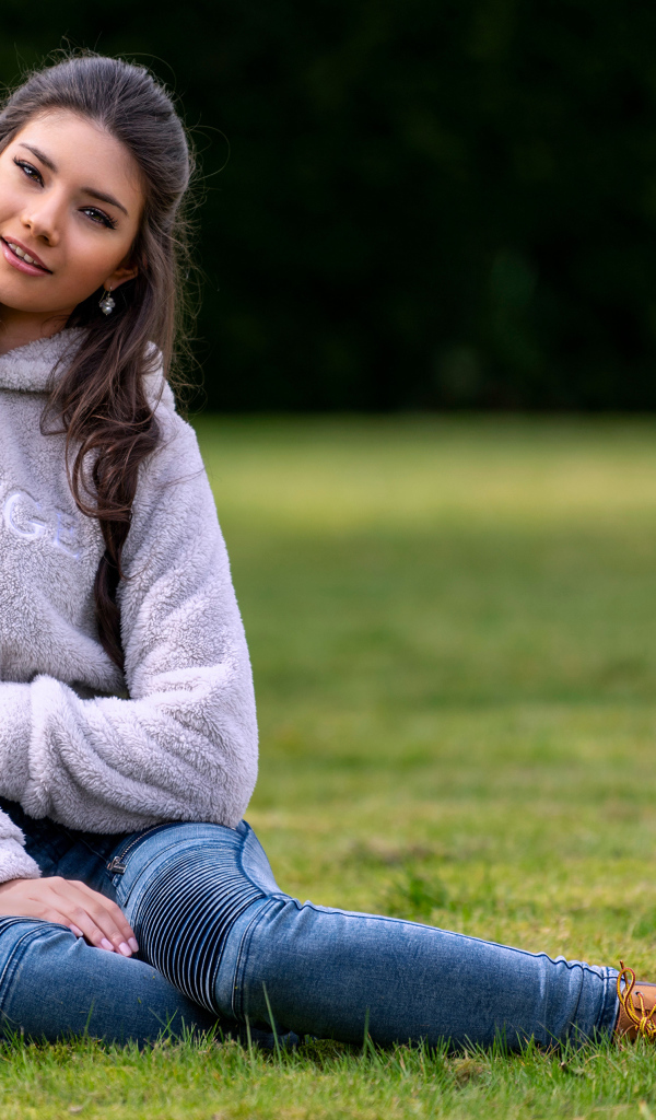 Молодая длинноволосая девушка сидит на траве 