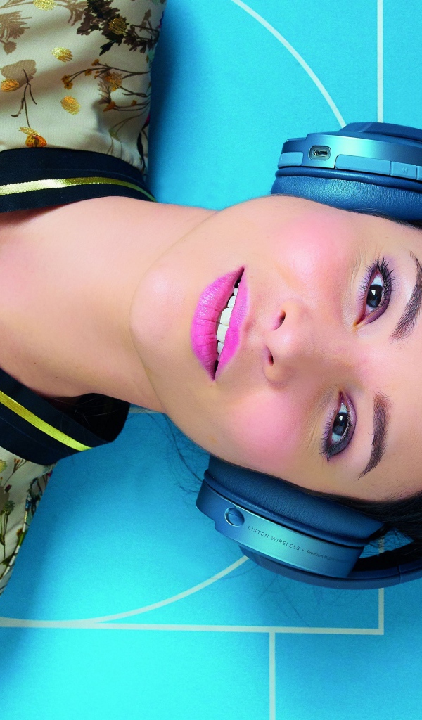 Молодая женщина в наушниках лежит на голубом полу