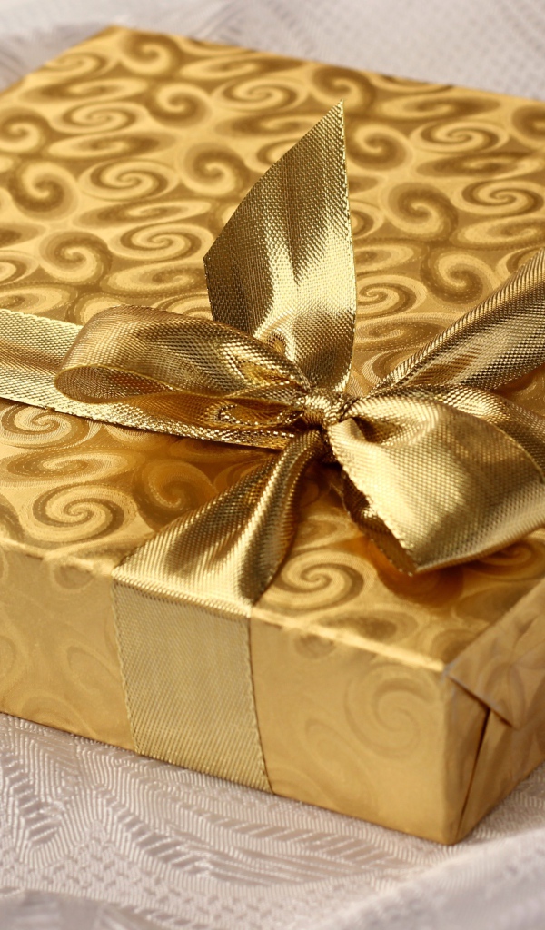 Красивая золотистая коробка с подарком на кровати 