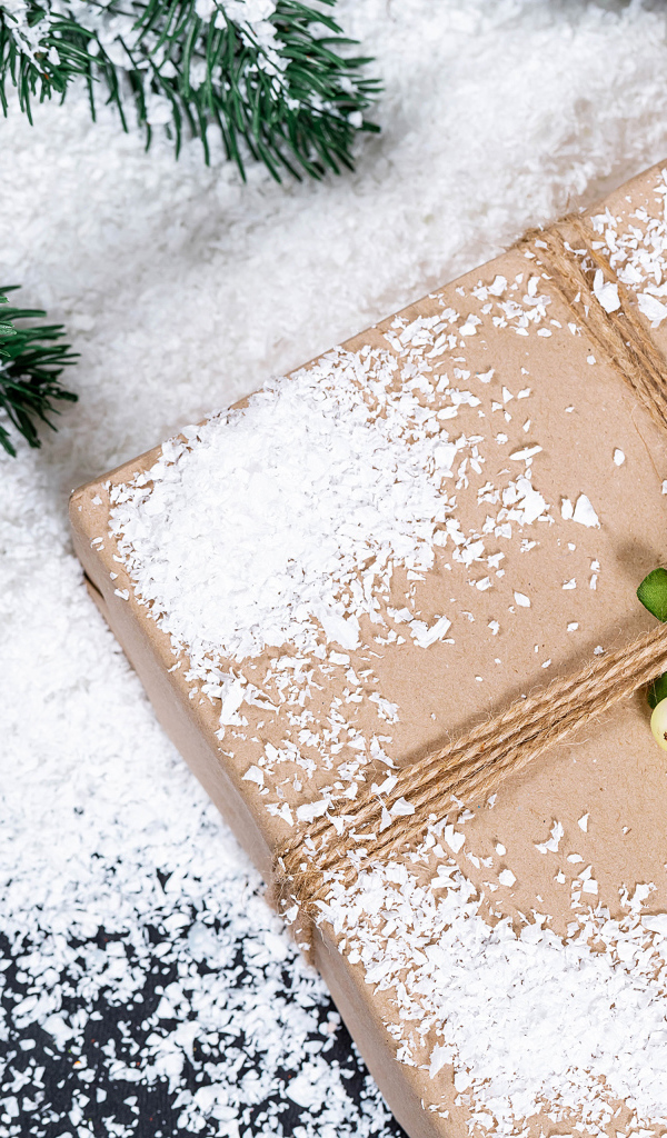 Подарок с заснеженной веткой ели на столе