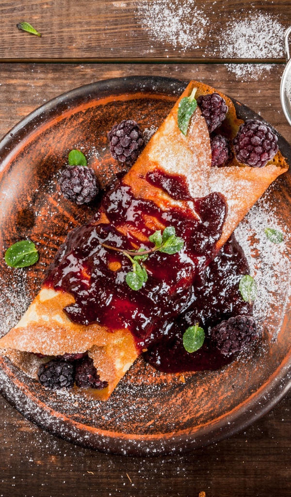 Блин с ягодами и джемом на тарелке с сахарной пудрой