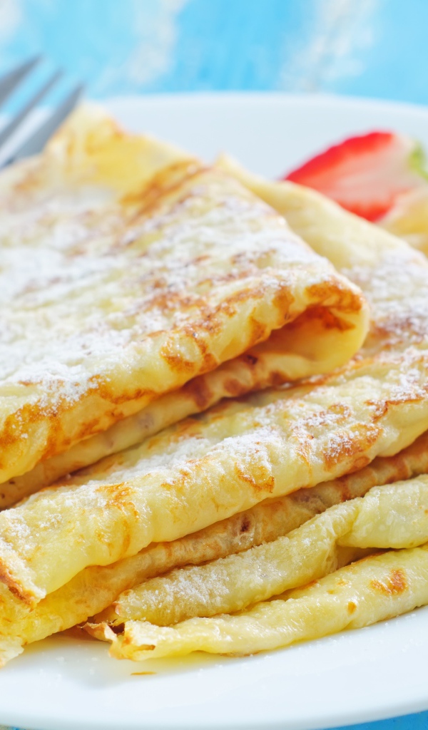 Румяные тонкие блинчики на тарелке с клубникой 