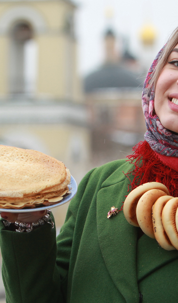 Улыбающаяся девушка с блинами и баранками на Масленицу