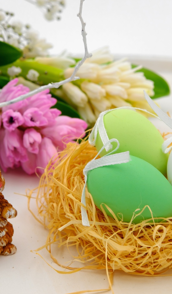 Три пасхальных яйца в гнезде на столе с цветами