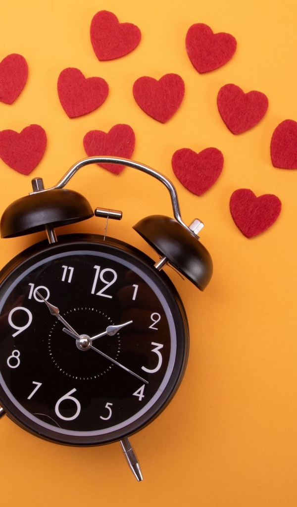 Black alarm clock with hearts on orange background