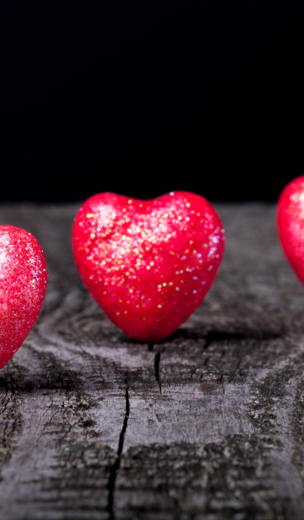 Блестящие красные сердечки на деревянном столе
