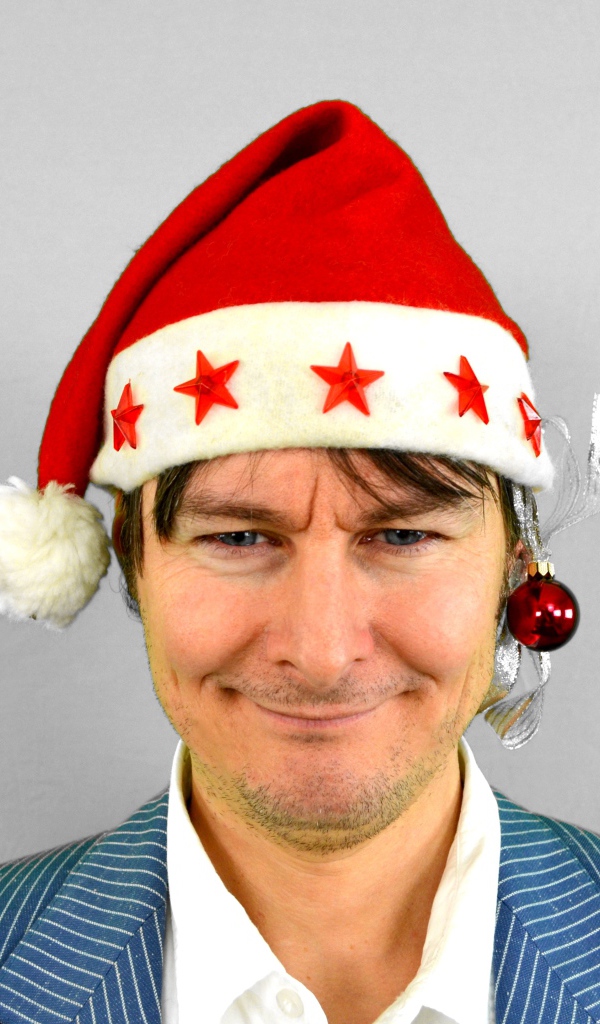 Голубоглазый мужчина в новогодней шапке на сером фоне 