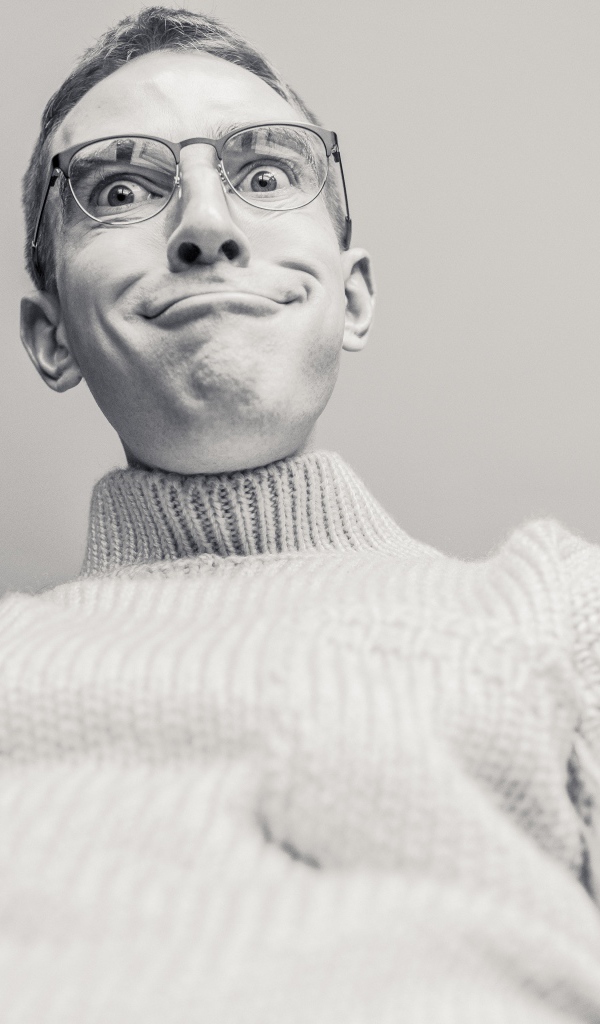 Мужчина в очках корчит лицо на сером фоне