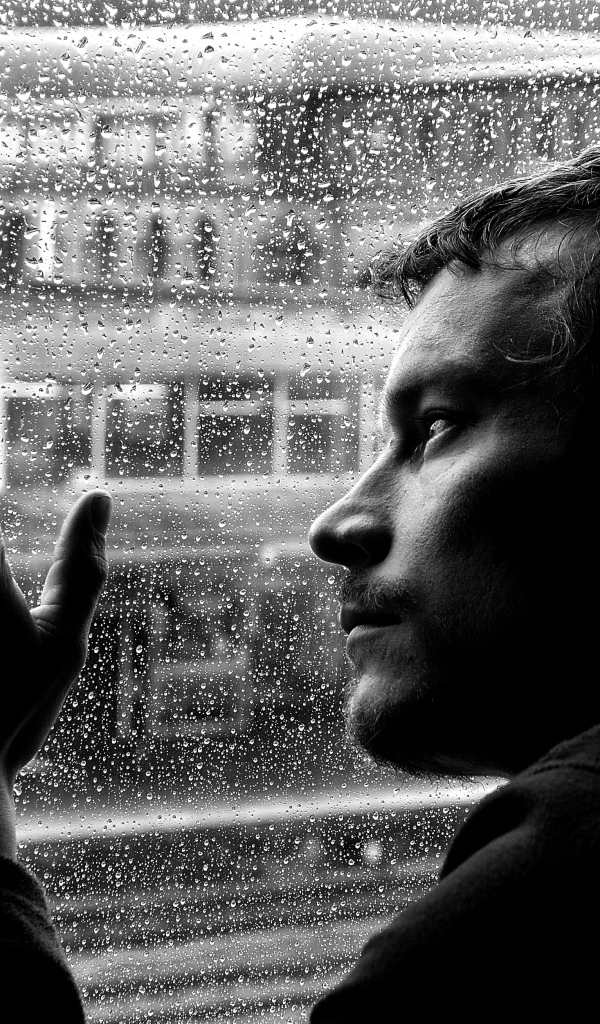 Грустный мужчина стоит у мокрого окна 