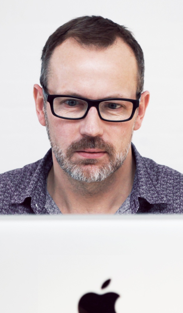 Серьезный мужчина в очках сидит за макбуком