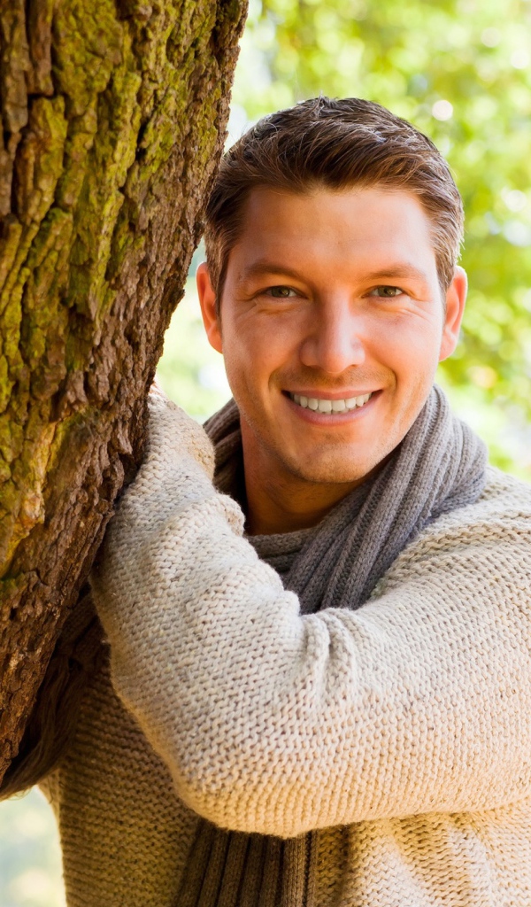 Улыбающийся мужчина стоит у дерева 