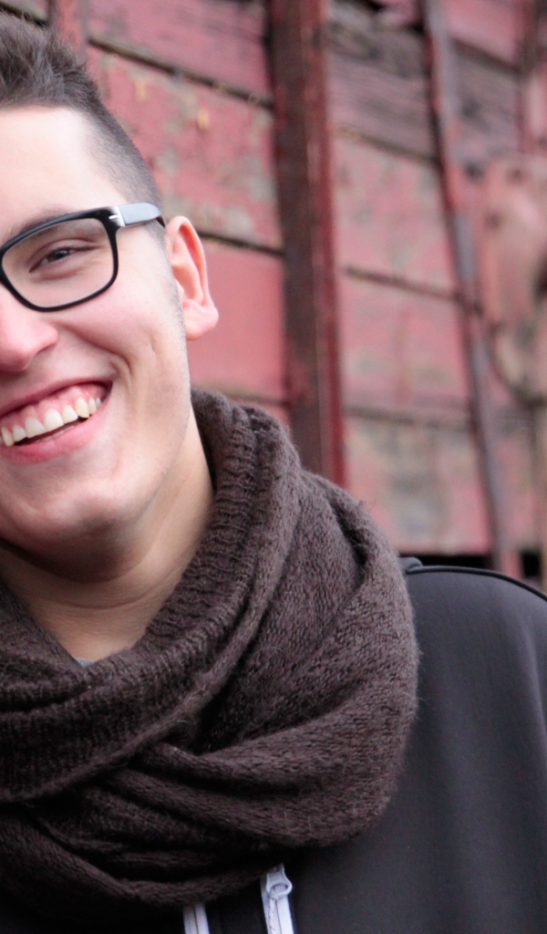 Улыбающийся мужчина в очках у стены 