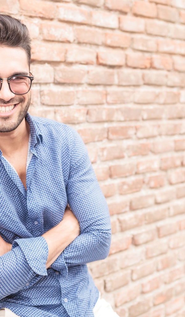 Улыбающийся мужчина в очках стоит у стены 