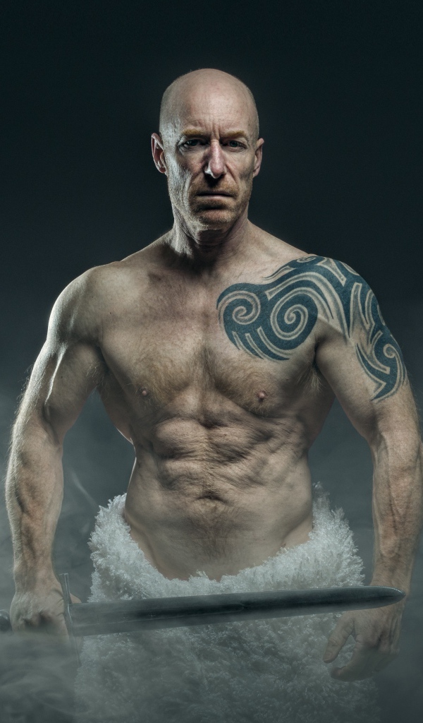 Сильный мужчина с мечом с татуировками на теле 