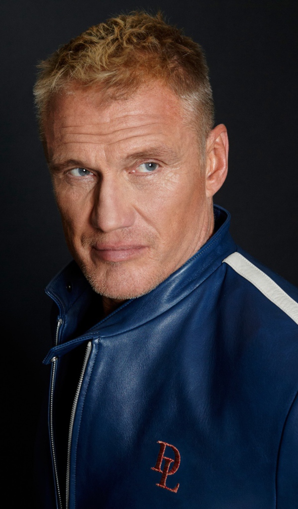 Актер Дольф Лундгрен в куртке на фоне  серой стены