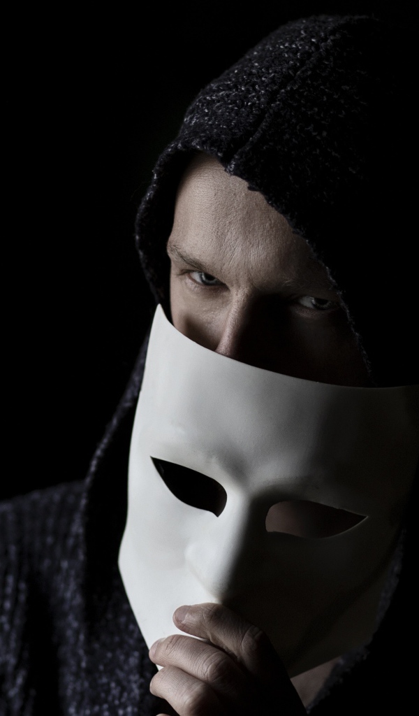 Мужчина прикрывает лицо белой маской на черном фоне