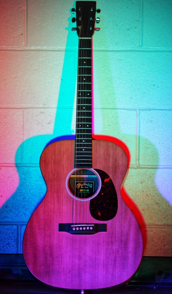 Гитара стоит у стены в разноцветном свете 