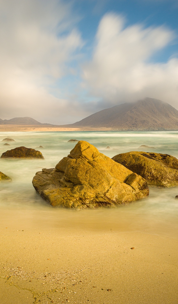 Большие камни лежат в воде на песке 