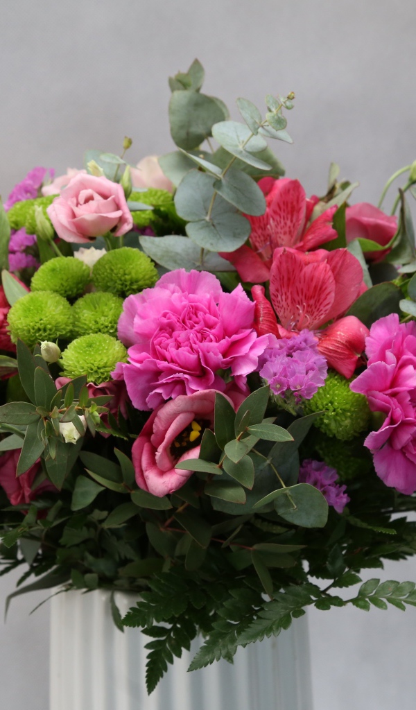 Красивый разноцветный букет в белой вазе на фоне серой стены 