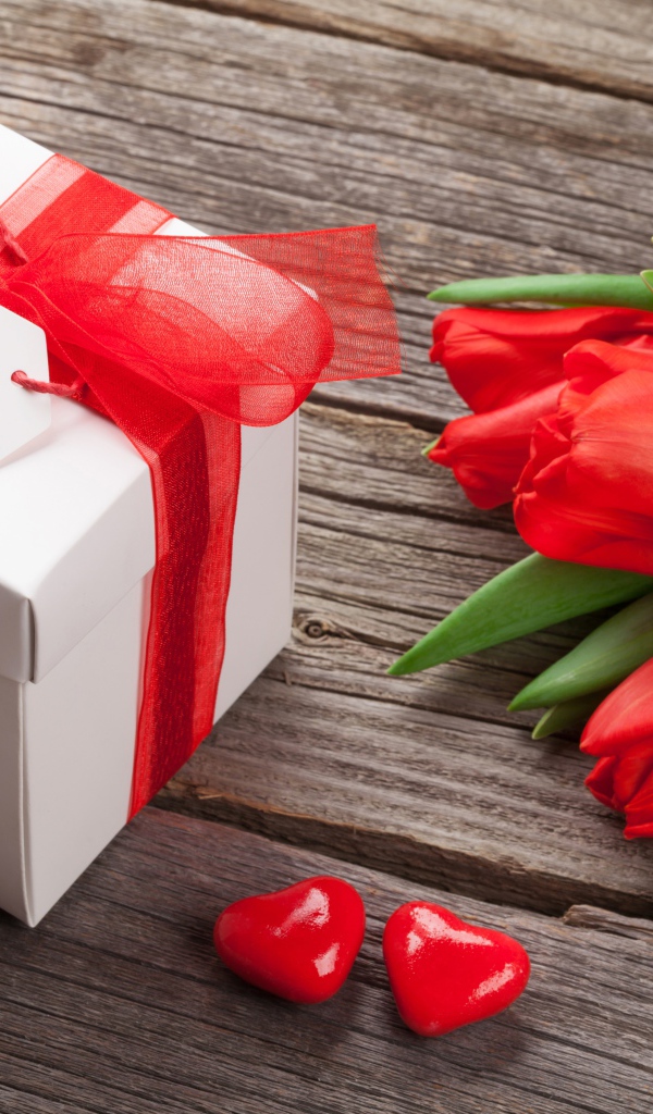 Красные тюльпаны с большим подарком на деревянном столе 
