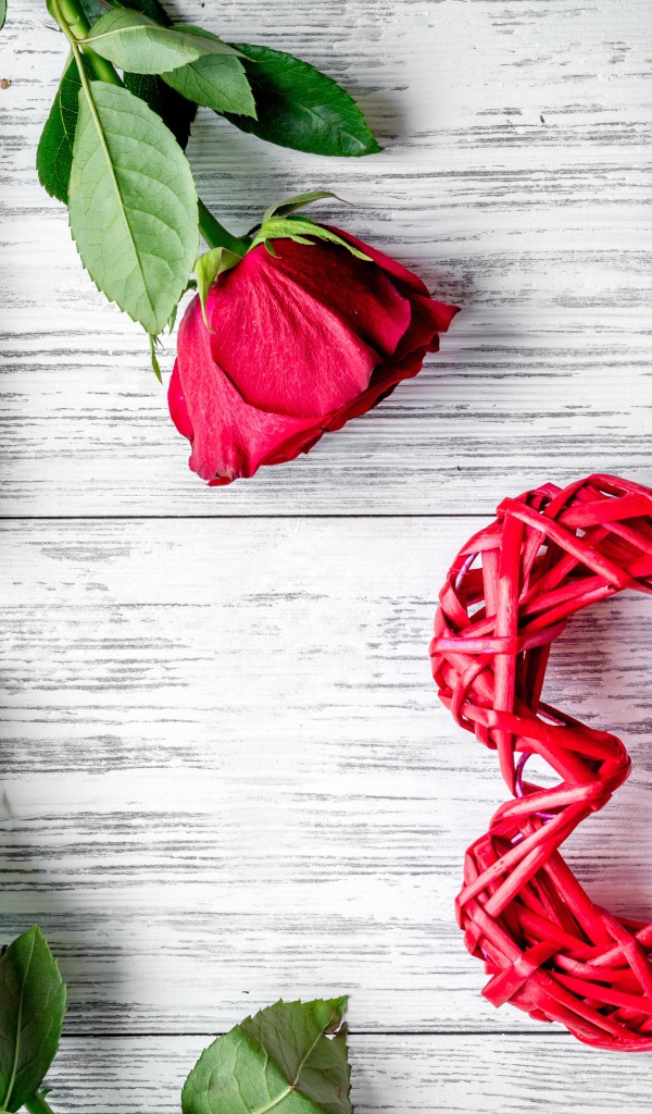 Красное плетеное сердце с алыми розами на деревянном столе