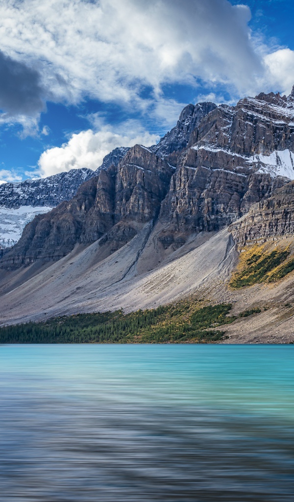 Высокие каменные горы в снегу под голубым небом у озера 