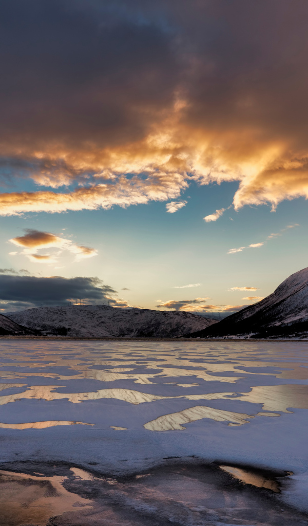 Покрытое льдом озеро у гор на закате солнца 