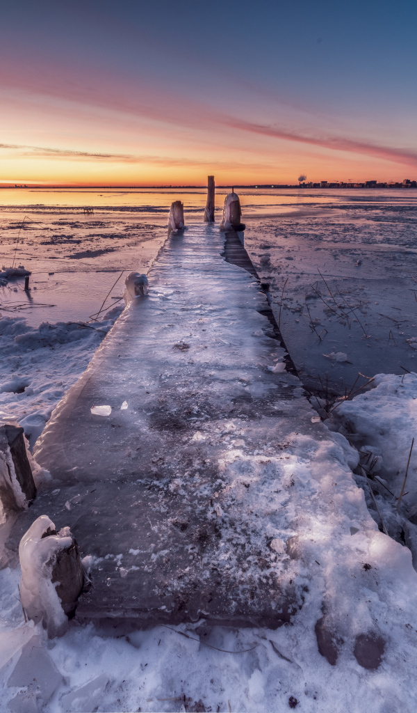 Покрытый льдом деревянный мост у озера 