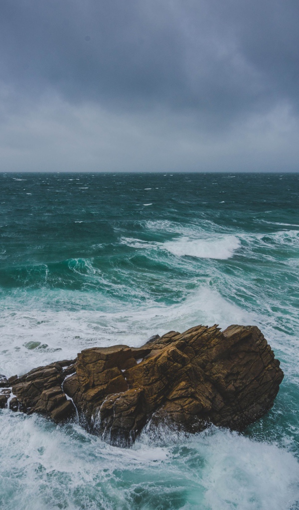 Большой камень омывают белые волны океана 