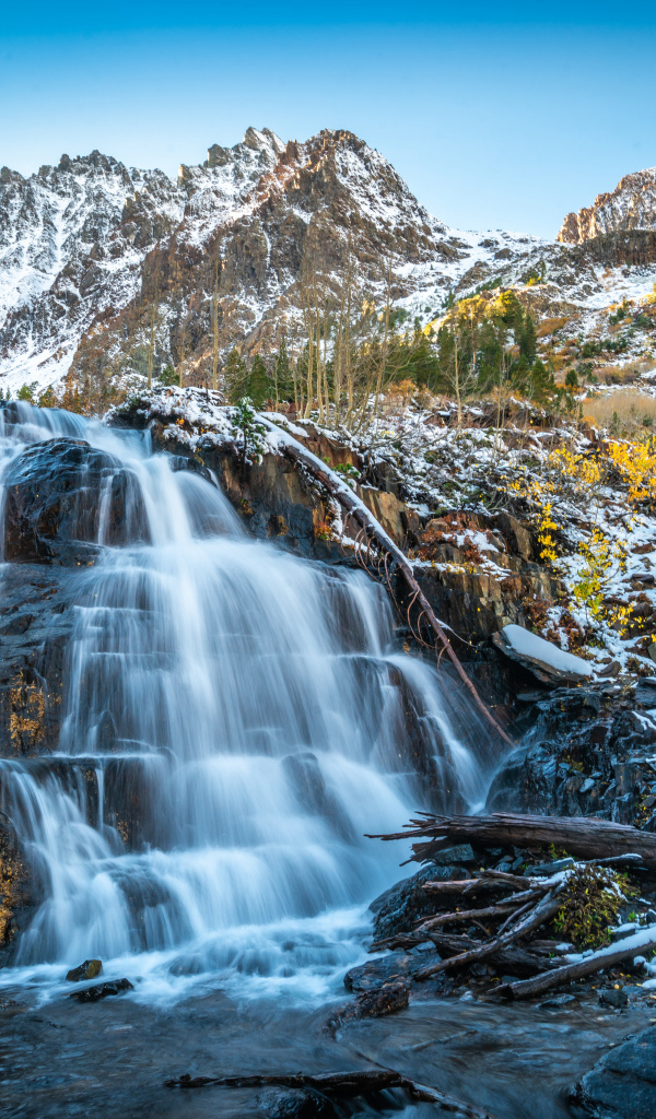 Красивый водопад стекает по холодным камням на фоне заснеженных гор