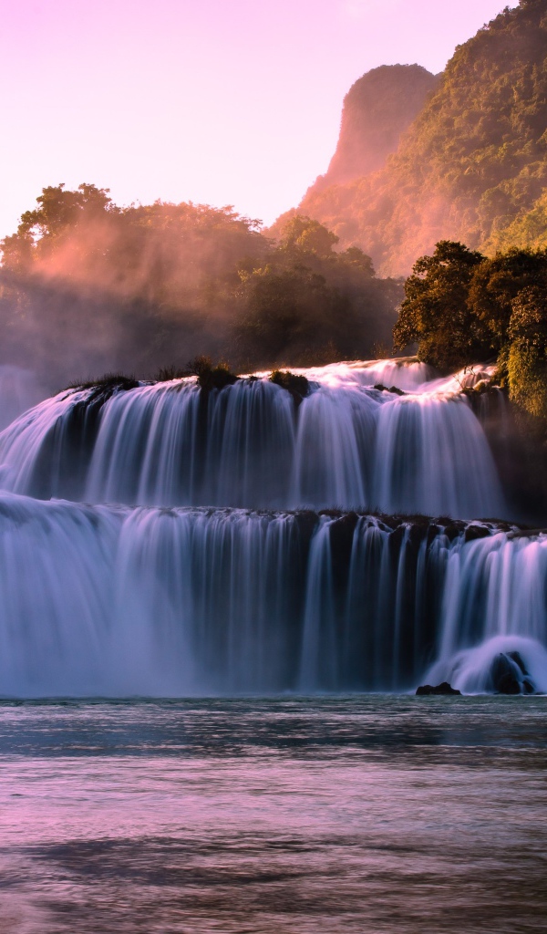 Каскадный водопад стекает по камням в лучах солнца 