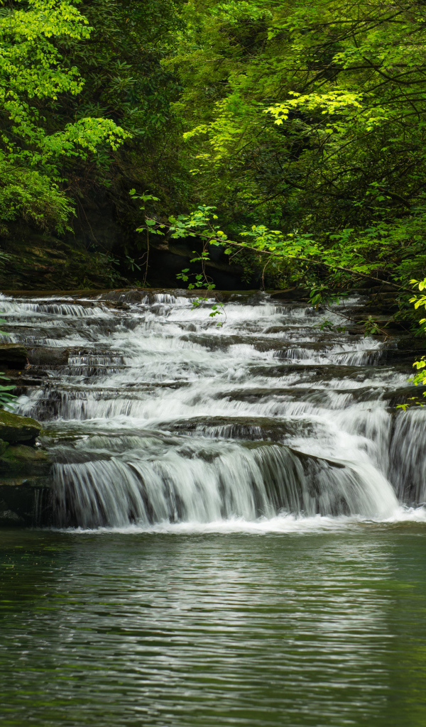 Водопад стекает по каменному каскаду в реку 