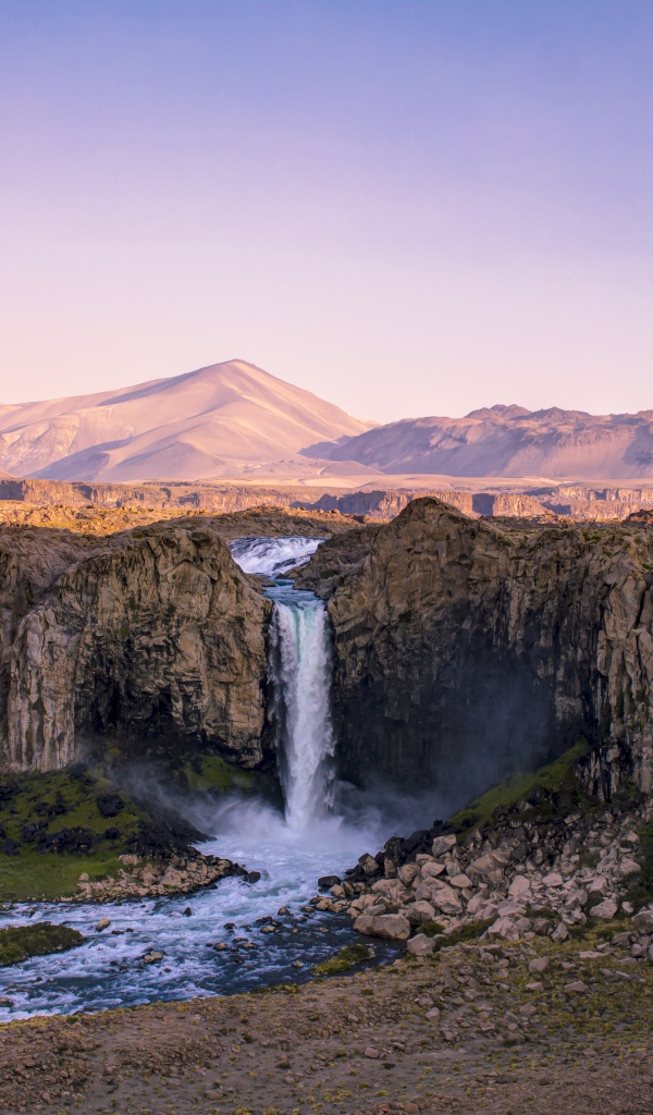 Водопад стекает по каменному склону горы на рассвете 