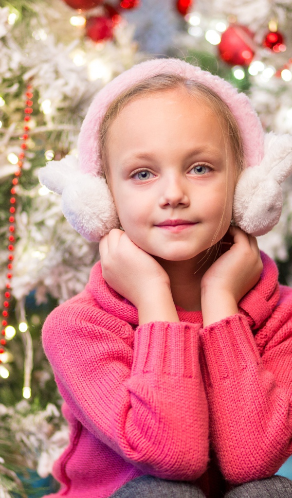 Девочка в розовых наушниках сидит у ели