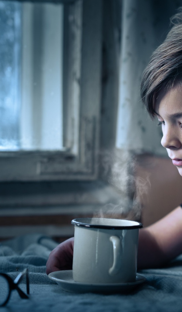 Маленький мальчик сидит за столом при свете свечи 