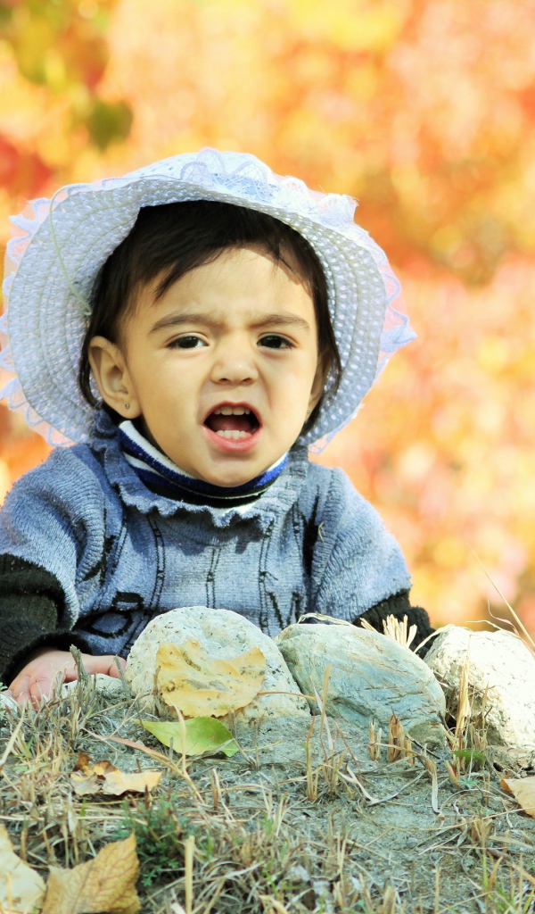 Маленькая девочка в шляпке сидит на земле