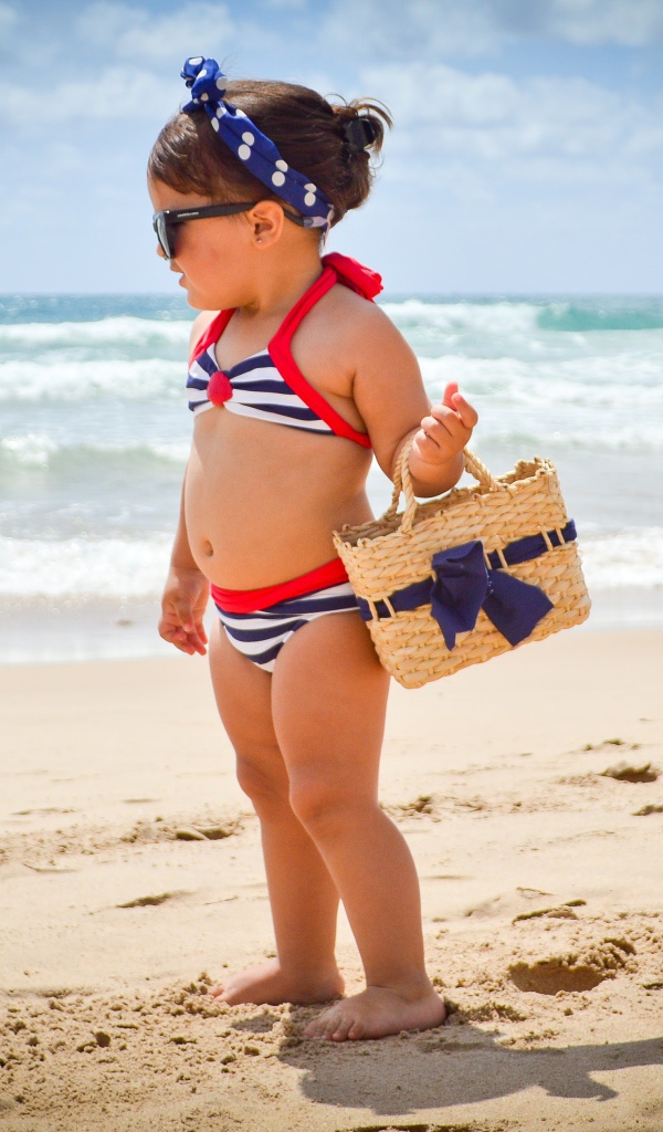 Маленькая девочка в купальнике гуляет по пляжу 