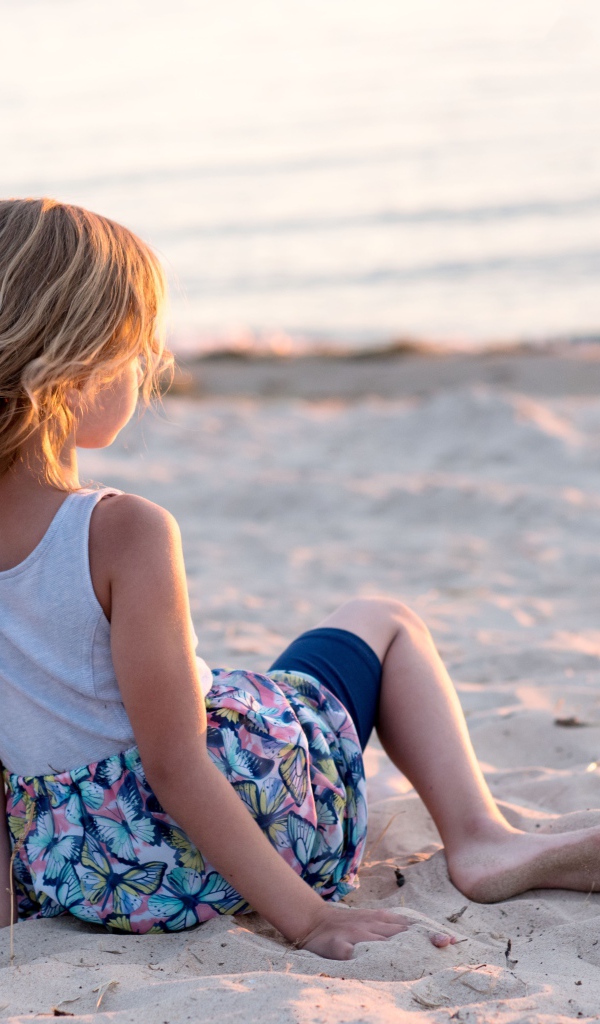 Маленькая девочка лежит на песке на закате 