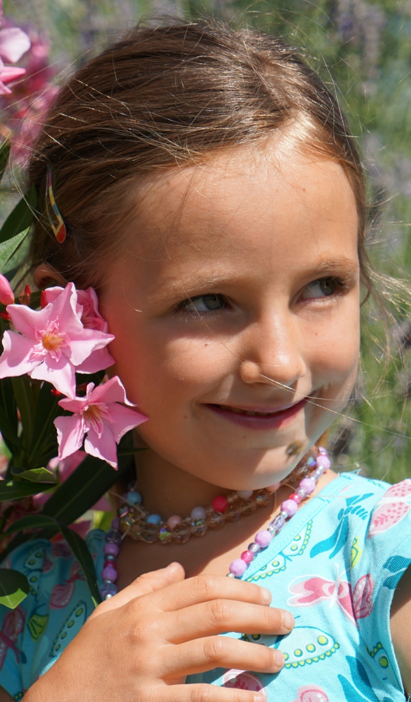 Маленькая девочка стоит у растения с розовыми цветами 