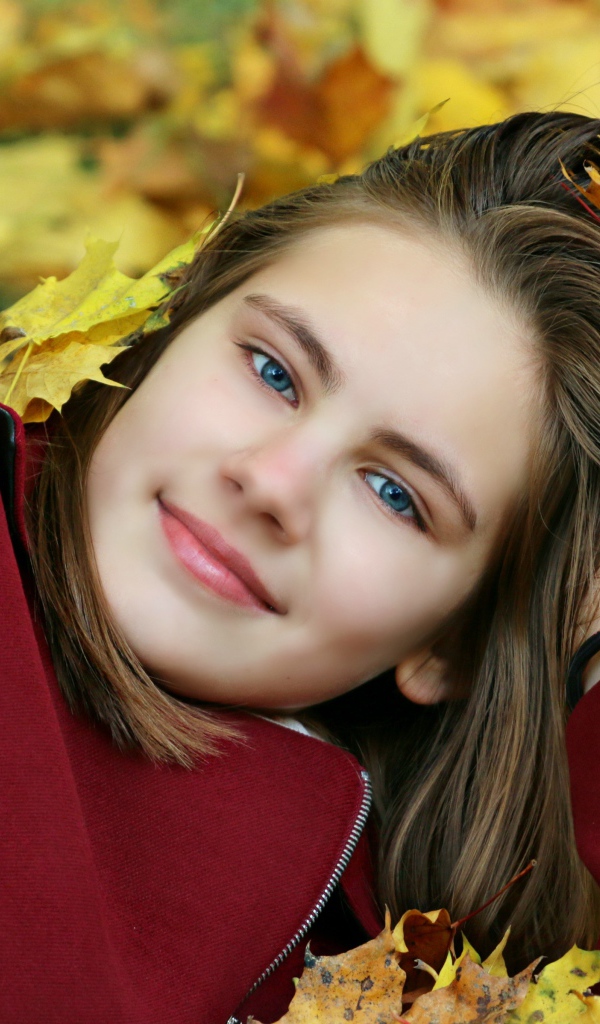 Красивая голубоглазая девочка лежит на опавшей листве
