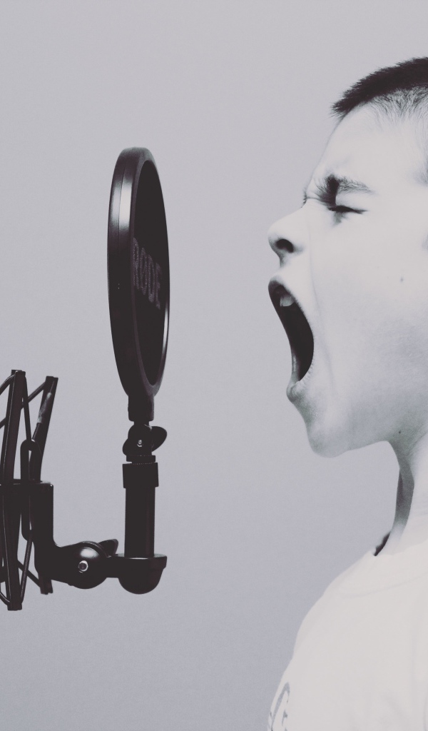 Мальчик кричит в студийный микрофон на сером фоне 