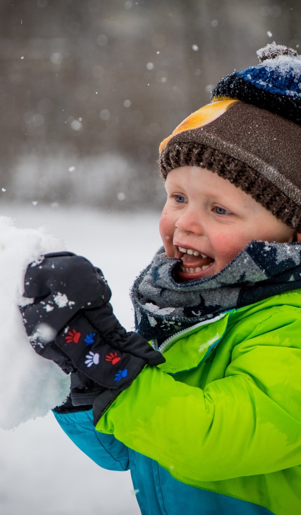 Веселый маленький мальчик со снегом в руках 