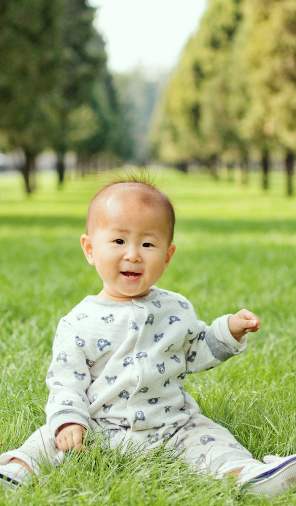 Маленький ребенок азиат сидит на зеленой траве 