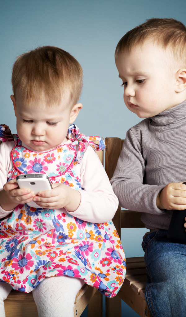 Маленькие мальчик  и девочка с телефонами на сером фоне 