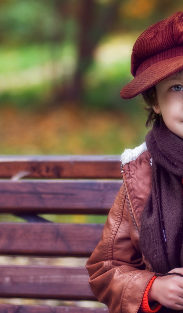 Маленький мальчик в кепке сидит на лавке