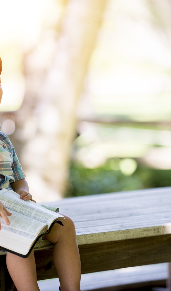 Маленький мальчик смеется на лавке с книгой