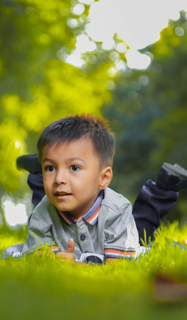 Маленький мальчик лежит на зеленой траве 