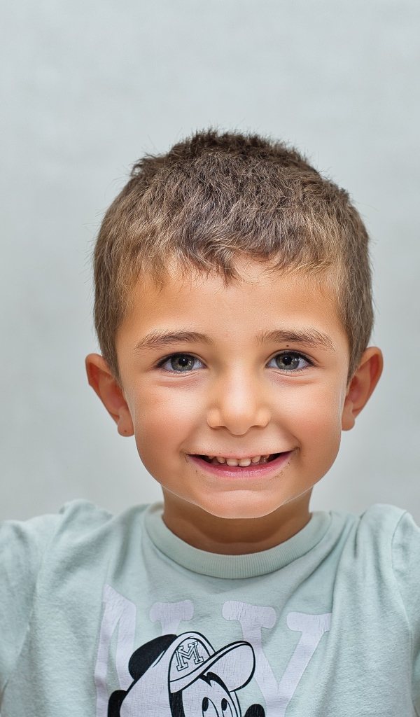 Маленький мальчик поднял руки вверх на сером фоне